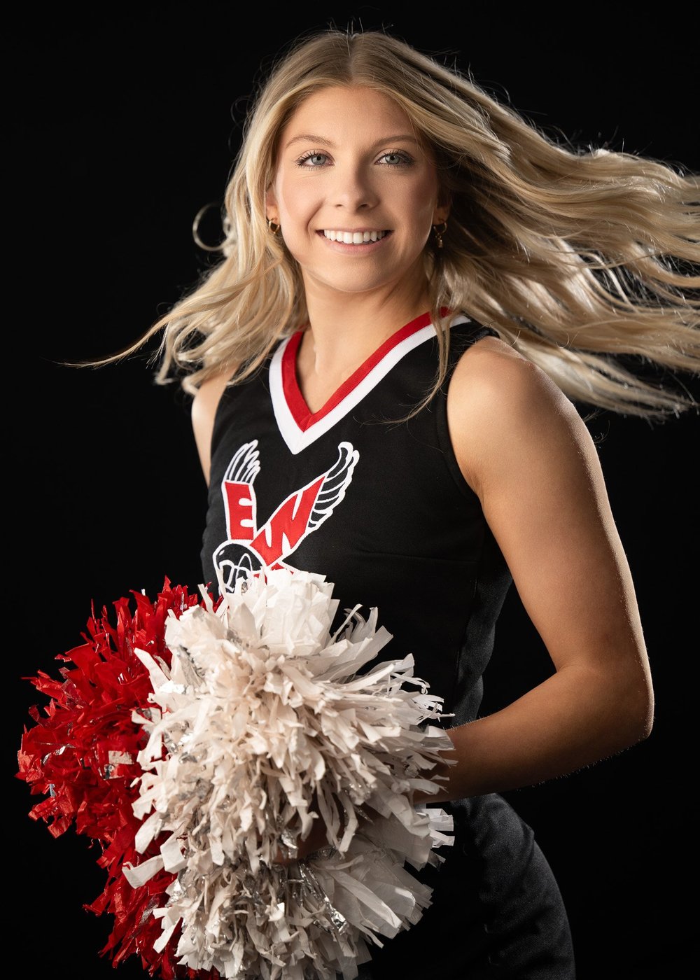 High school cheerleader in uniform posing with pom poms in the studio