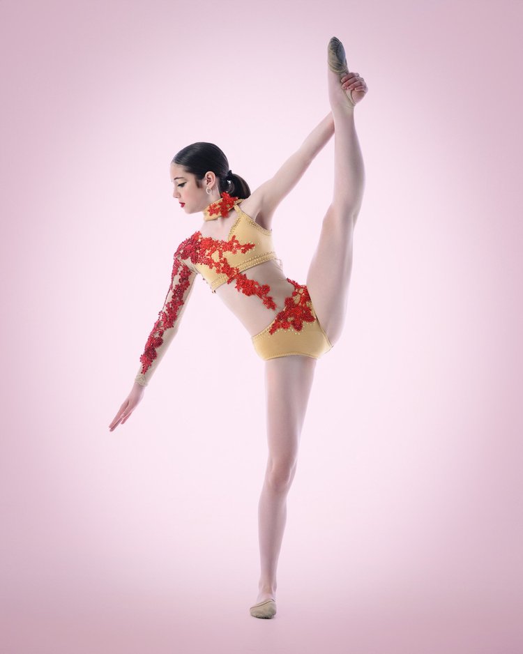 Dancer in a red and gold costume holding a standing leg extension in the studio